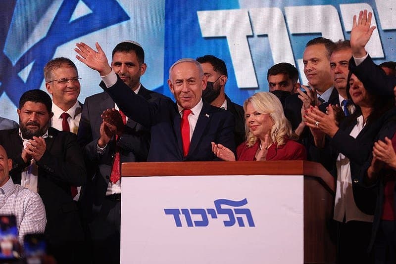 Benjamin Netanyahu waves at a campaign event as supporters applaud.